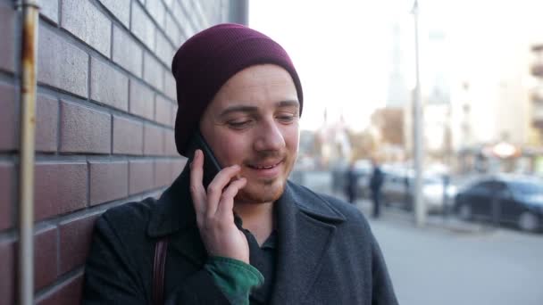 Joven hombre solitario hablando por teléfono cerca de la pared de ladrillo en la ciudad — Vídeos de Stock