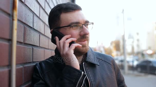 Молодий самотній чоловік говорить по телефону біля цегляної стіни в місті — стокове відео