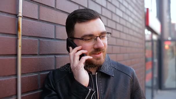 Молодий самотній чоловік говорить по телефону біля цегляної стіни в місті — стокове відео