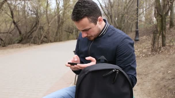 Ung man spelar beröring skärm telefonerna i parken — Stockvideo