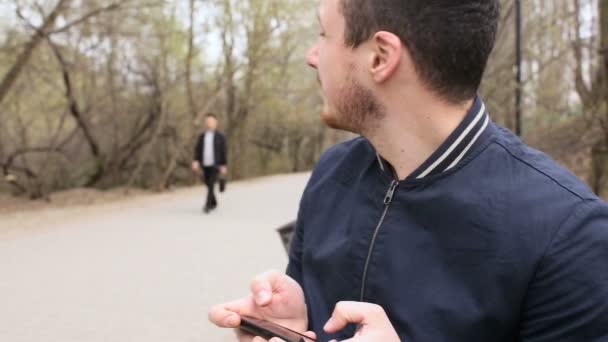 Joven jugando al teléfono con pantalla táctil en el parque — Vídeo de stock