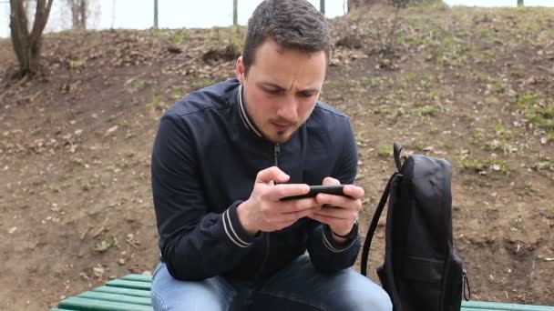 Młody człowiek w ekran dotykowy telefon w parku — Wideo stockowe