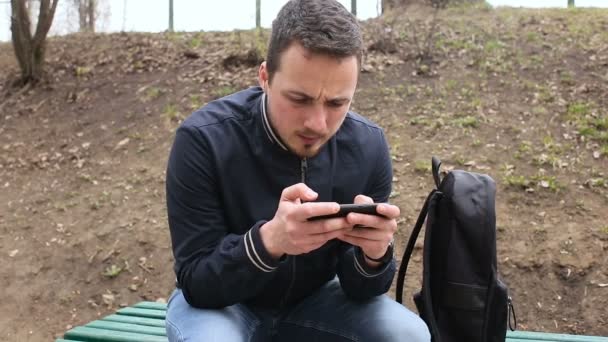 Jovem jogando telefone touch screen no parque — Vídeo de Stock