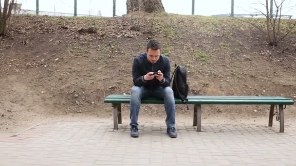 Молодой человек играет на сенсорном экране телефона в парке — стоковое видео