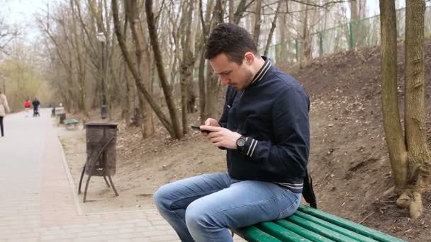 Hombre sentado en el banco del parque con teléfono móvil — Vídeo de stock