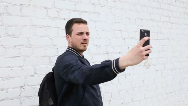 Jovem bonito cara fazendo selfie perto de parede de tijolo branco — Vídeo de Stock