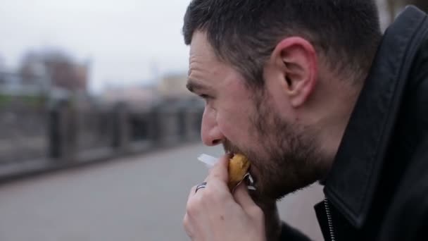 Adult alone man eat hotdog in the city on a bench — Stock Video