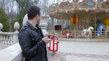 Genç adam parkta bir atlıkarınca arka plan üzerinde cep telefonu kullanmak