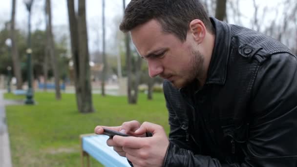 Alleen man spelen op telefoon in het park — Stockvideo