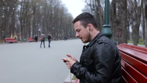 Hombre moderno escuchar música en el teléfono inteligente en el parque de la ciudad — Vídeo de stock