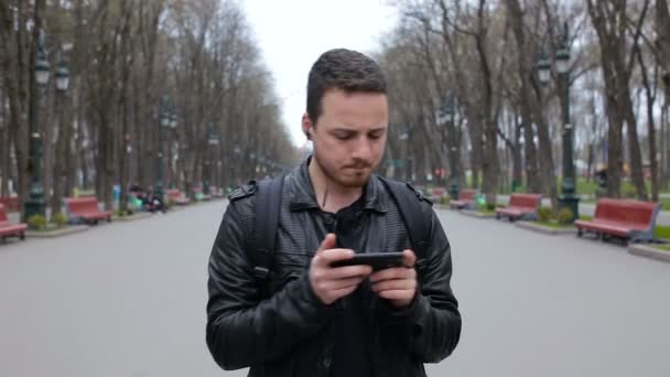 Joven hombre de moda escuchar música en el teléfono inteligente en el parque de la ciudad y bailar — Vídeo de stock