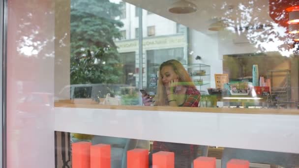 モダンなカフェで音楽を聴いている女の子。通りの車は窓の反射 — ストック動画