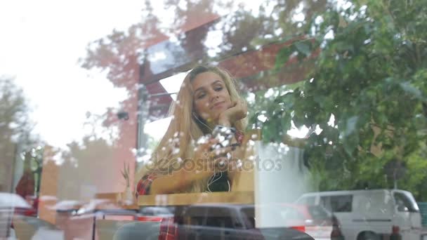 Menina ouvindo música no café moderno. O tráfego de rua está na janela de reflexão — Vídeo de Stock