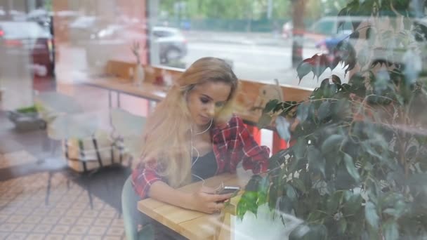 Mädchen hören Musik in einem modernen Café. Straßenverkehr spiegelt sich wider — Stockvideo