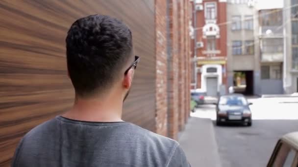 De man loopt rond de stad in de buurt van de bakstenen muur — Stockvideo