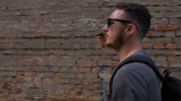 Un joven camina frente a una pared de ladrillo — Vídeos de Stock