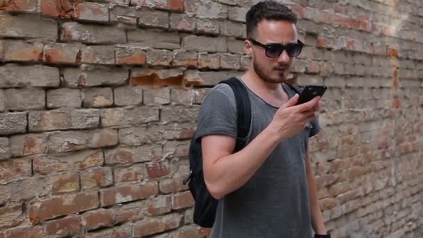 O tipo usa um smartphone perto de uma parede de tijolos. Slo tiro movimento — Vídeo de Stock