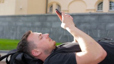 Genç bir adam şehirde bir bankta bir telefon kullanır