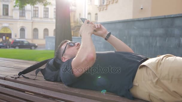 Un jeune homme utilise un téléphone sur un banc de la ville — Video