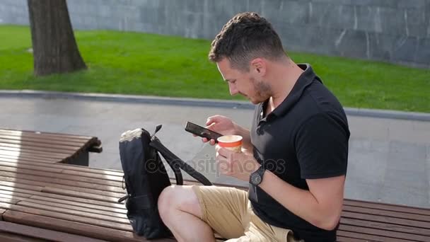 ein junger Mann sitzt auf einer Bank und trinkt draußen in der Stadt Kaffee