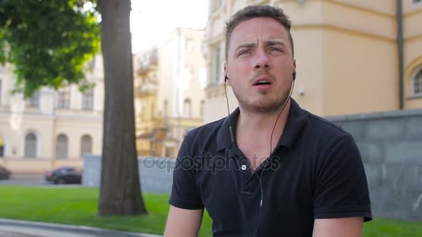 A fiatalember beszél a mobiltelefon egy padon a városban — Stock videók