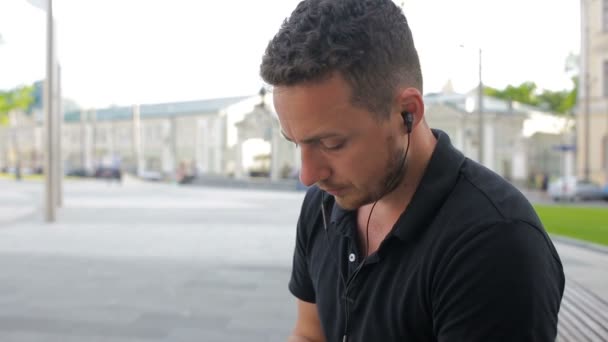 Jonge man praten op mobiele telefoon op een bankje in de stad — Stockvideo