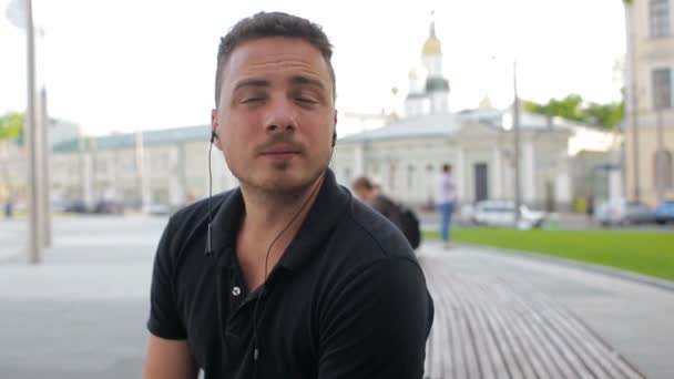 A fiatalember beszél a mobiltelefon egy padon a városban — Stock videók