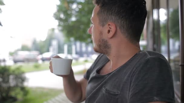 Een man drinkt koffie in een café en kijkt rond — Stockvideo