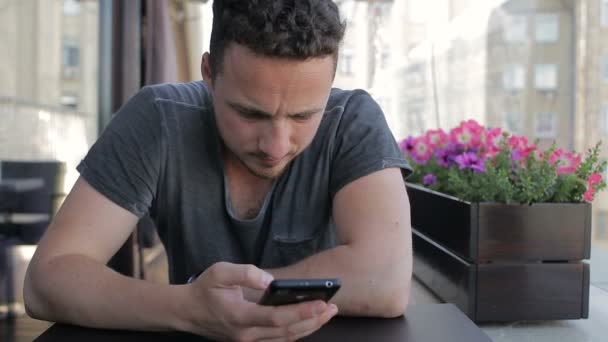 Молодий чоловік зі смартфоном в кафе — стокове відео