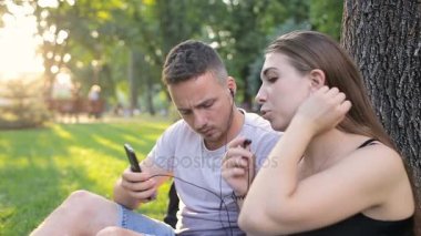 Adam ve kız bir ağacın altında bir parkta telefonda müzik dinlemek