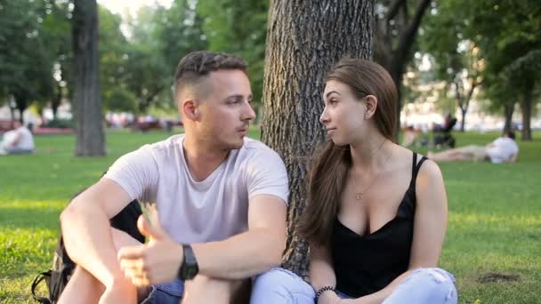 Um tipo com uma rapariga a falar num parque debaixo de uma árvore — Vídeo de Stock