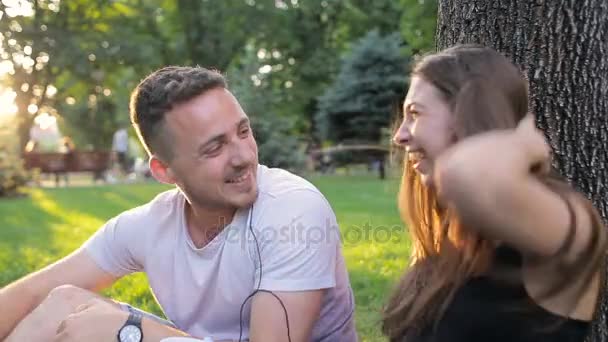 男と女、ツリーの下に座って公園の音楽に合わせて踊る — ストック動画
