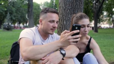 Adam kız şakalar telefonda bir ağacın altında bir parkta otururken gösterir