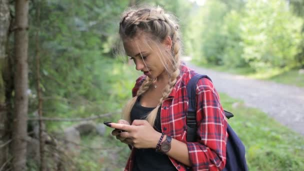 Счастливая девушка стоит в лесу и пишет смс на смартфоне — стоковое видео