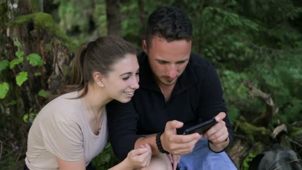 Una joven pareja de mochileros descansando en el bosque y usando un teléfono inteligente — Vídeos de Stock