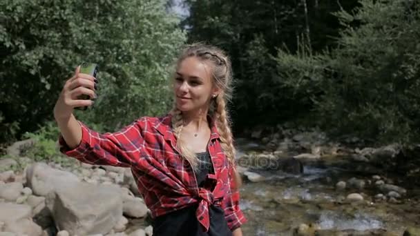 Красивая блондинка делает селфи возле горного ручья — стоковое видео