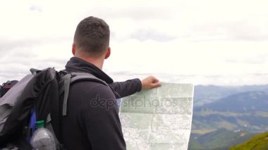 Genç adam turist bir harita bir dağın tepesinde kullanır.