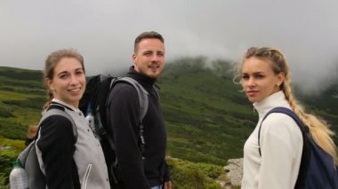 Bir adam ve iki seyahat kız kameranın arka planı dağlar ve sis bakmak