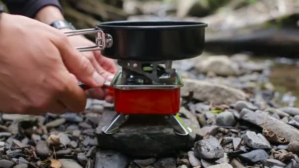 Mens handen zet een koekenpan op een toeristische fakkel op een camping vlakbij een rivier — Stockvideo