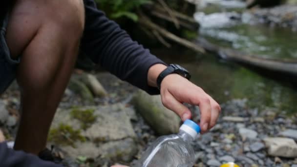 El hombre vierte aceite en una sartén al aire libre en un camping cerca del río — Vídeo de stock