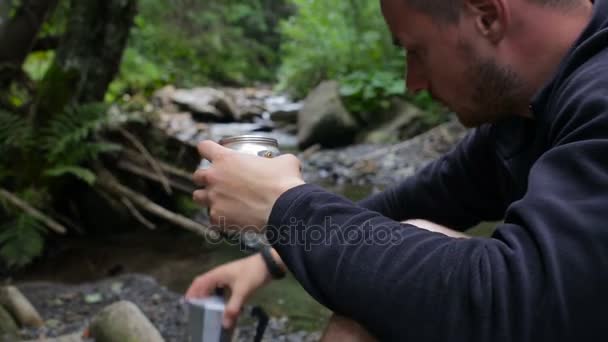 Un turista vierte agua en una cafetera en un camping en la orilla del río — Vídeo de stock