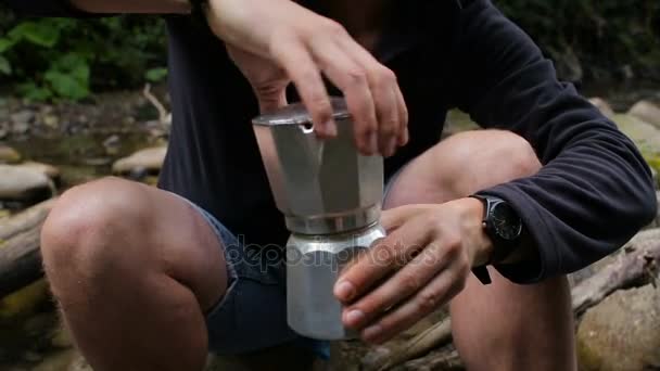 Ein Mann kocht Kaffee in einer Kaffeemaschine auf einem Campingplatz am Flussufer — Stockvideo