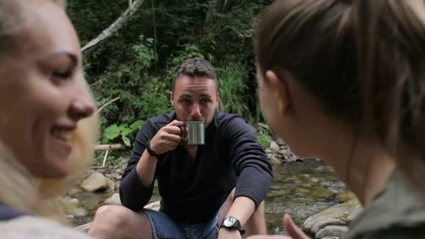 Los excursionistas toman café en el campamento cerca del arroyo — Vídeos de Stock