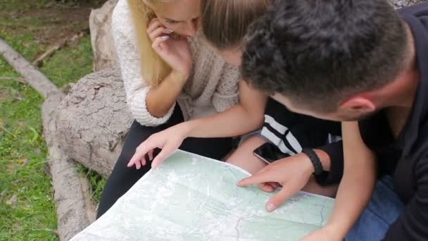 Freunde Reisende erkunden die Karte und die Route auf einem riesigen Baumstamm sitzend — Stockvideo