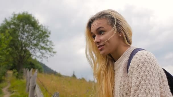 Hermosa chica hablando con alguien y sonriendo al fondo del bosque y pueblo de montaña — Vídeo de stock