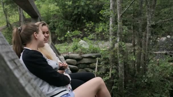 Les jeunes filles sont assises sur un pont à travers une rivière de montagne — Video