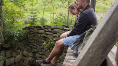 Genç çift turist ile bir dağ nehir üzerinde bir köprüde siting sırt çantaları