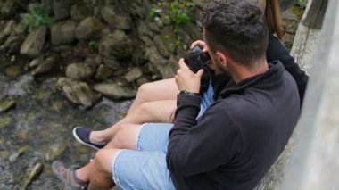 Turist bir dağ nehir üzerinde bir köprü üzerinde sırt çantaları ile genç bir çift. Nehir üzerinde arka plan ayak bir fotoğraf olun