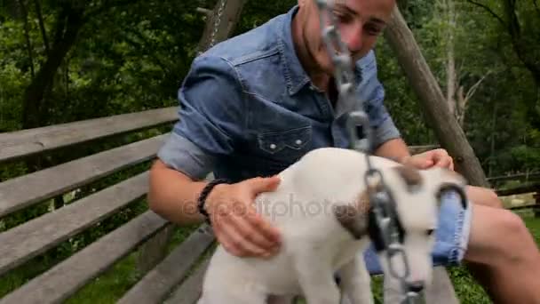 Ένας άντρας με ένα σκύλο να κουνιέστε σε μία κούνια στο κατώφλι — Αρχείο Βίντεο