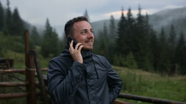 Un joven está hablando por teléfono por la noche en las montañas. Alrededor del bosque en la niebla — Vídeo de stock